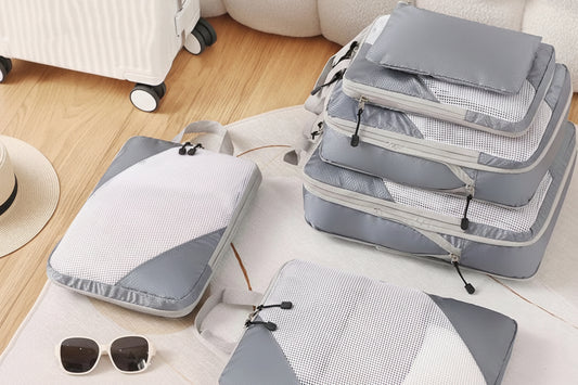 Set of gray compression packing cubes filled with clothes ready for travel, sitting on a light surface with sunglasses nearby.