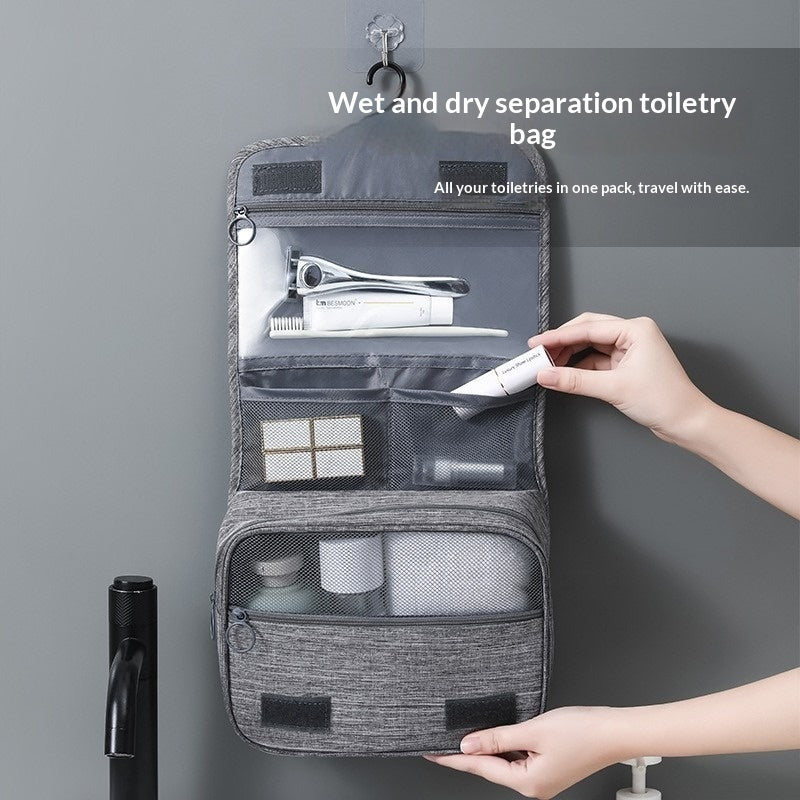 Gray toiletry bag with compartments, hung on a hook on a grey wall. The bag is opened up to show multiple compartments including zipper enclosed sections and mess elastic sections. 