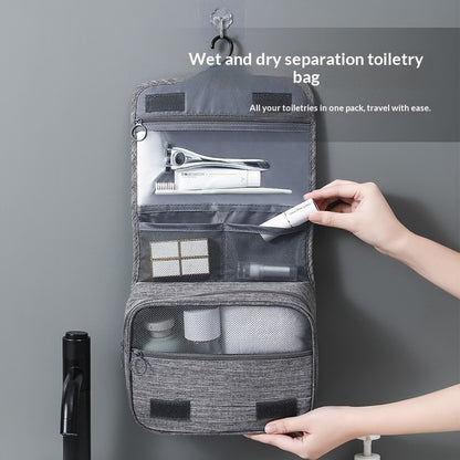Gray toiletry bag with compartments, hung on a hook on a grey wall. The bag is opened up to show multiple compartments including zipper enclosed sections and mess elastic sections. 